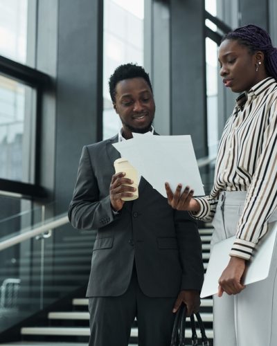 Graphic waist up portrait of two African-American business people discussing documents while standing in office hall, copy space