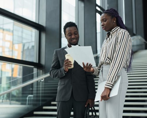 Graphic waist up portrait of two African-American business people discussing documents while standing in office hall, copy space